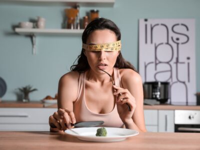 a woman eating broccoli blindfolded with body measuring tape